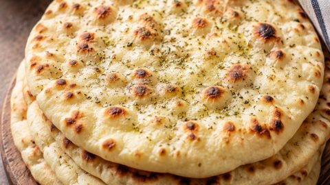 Grčki pita hleb složen na drvenoj dasci uz caciki, masline, feta sir i maslinovo ulje.