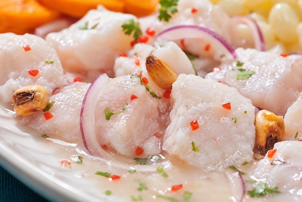 Krupni kadar peruanskog cevichea od brancina u leche de tigre sa crvenim lukom, ají limo papričicom i canchom