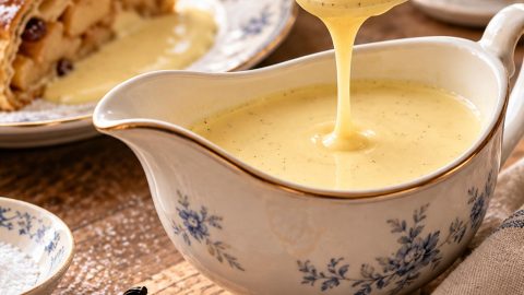 Bečki sos od vanile (Vanillesauce) u porcelanskoj posudi, sa vidljivim semenkama prave vanile i kašikom koja pokazuje njegovu svilenkastu teksturu.