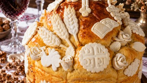 Mrsni slavski kolač sa zlatnom korom i tradicionalnim belim ukrasima od testa, poslužen na svečanom stolu uz vino i slavsku sveću.